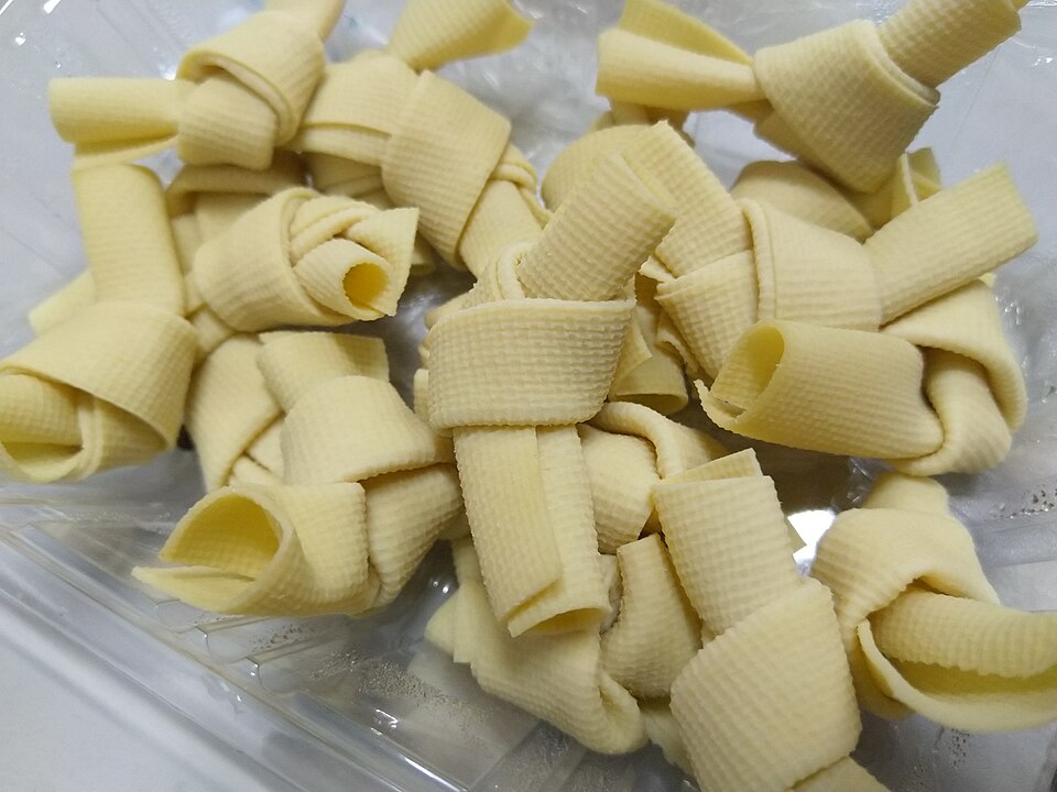 Pale yellow thin bean-curd sheets tied into knots, showing a woven grid texture