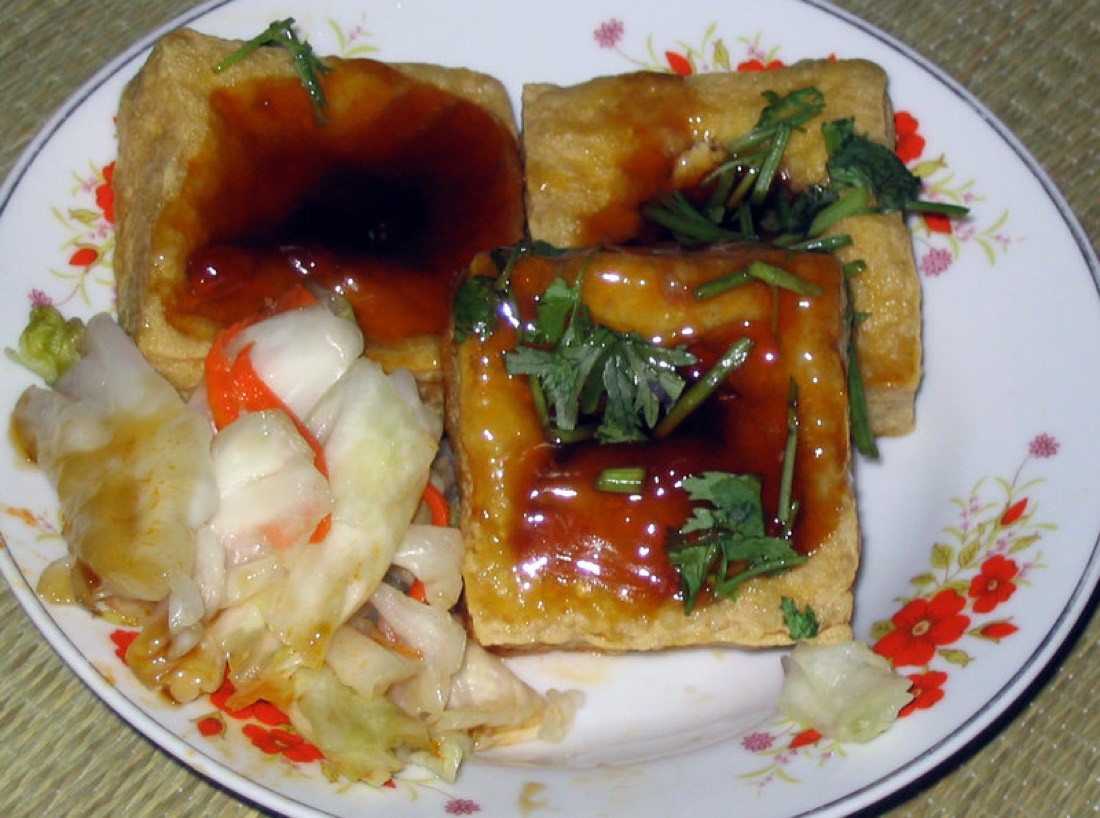 Fried stinky tofu squares with cupped tops holding sauce, served with pickled cabbage