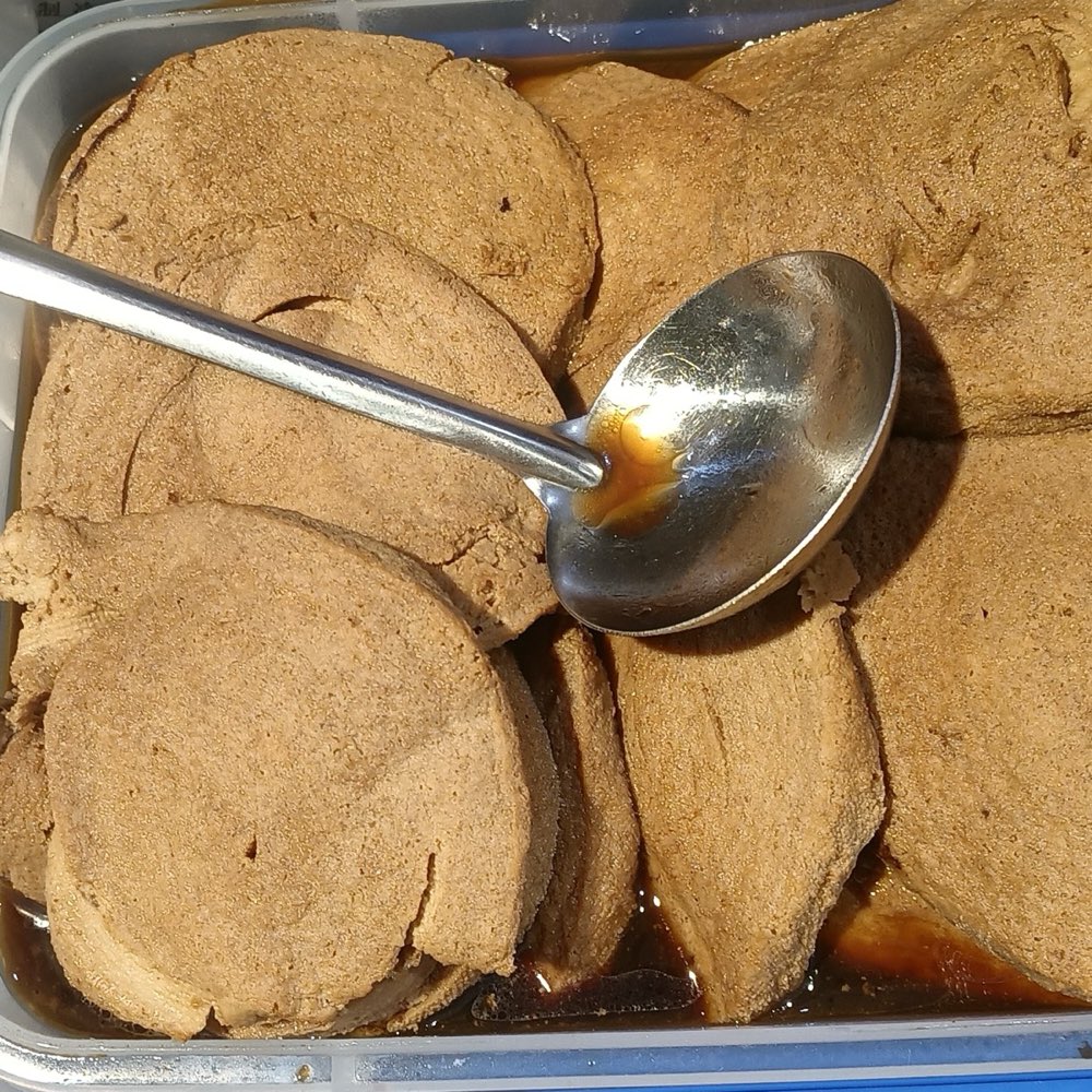 Sliced soy-braised vegetarian chicken rounds sitting in braising liquid with a ladle